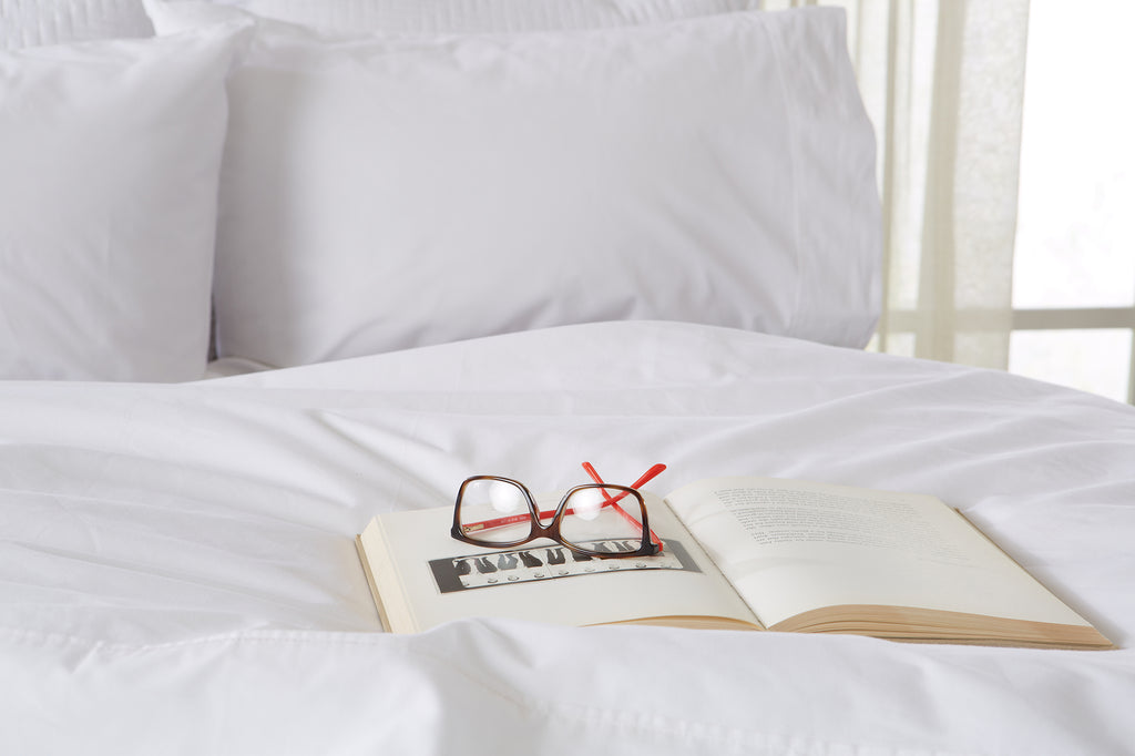 Glasses sit on top of a book on a bed.